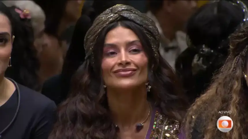 Aline Campos sentada no sofá da sala pouco antes da eliminação no BBB 26. Ela mexe a boca com semblante triste