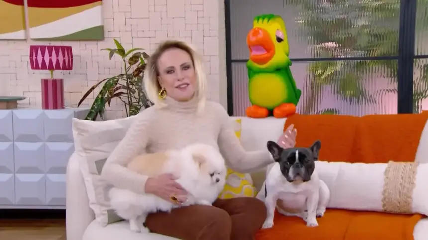 Ana Maria Braga sentada no sofá ao lado de dois cachorros e do Louro Mané na chamada do Mais Você