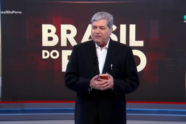 Datena segura telefone celular nas mãos em frente ao telão com o logo do Brasil do Povo no cenário da RedeTV!