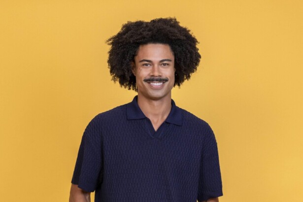 Breno sorridente em um fundo amarelo na divulgação do BBB 26