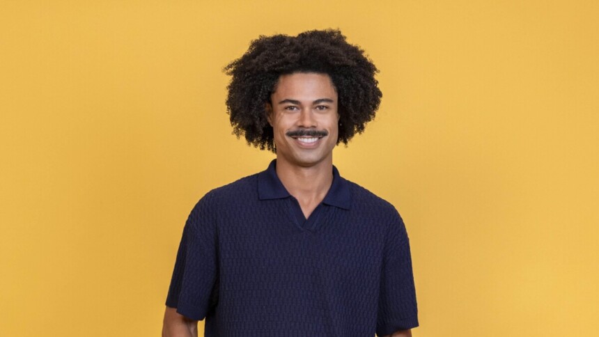 Breno sorridente em um fundo amarelo na divulgação do BBB 26