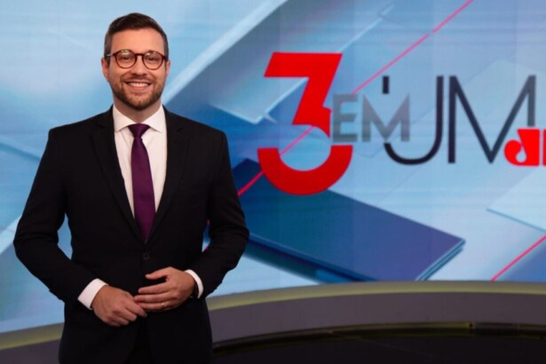 Cassius Zeilmann, de terno e sorrido, posando no cenário do 3 en 1 da Jovem Pan