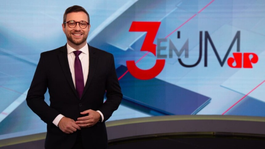 Cassius Zeilmann, de terno e sorrido, posando no cenário do 3 en 1 da Jovem Pan