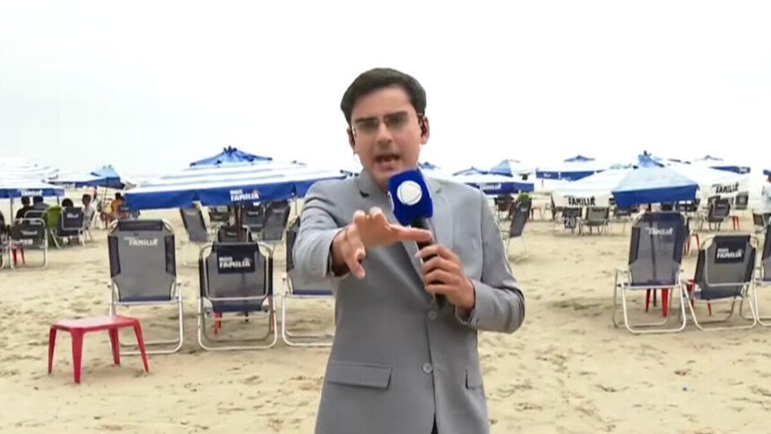 Dudu Camargo vestindo um terno cinza e microfone da RECORD na mão, em trecho de participação ao vivo no Balanço Geral