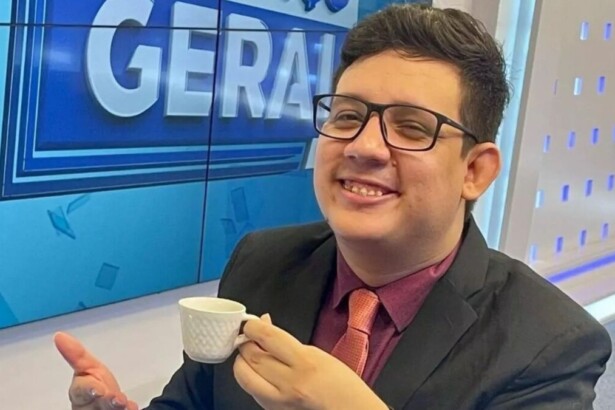 Erlan Bastos sorrindo com uma xícara na mão no estúdio do Balanço Geral
