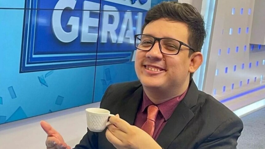 Erlan Bastos sorrindo com uma xícara na mão no estúdio do Balanço Geral