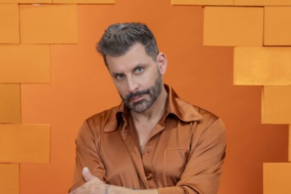Henri Castelli veste roupa laranja e olha com olhar sério em foto oficial do BBB 26