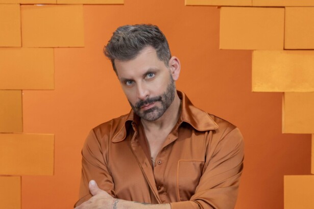 Henri Castelli veste roupa laranja e olha com olhar sério em foto oficial do BBB 26