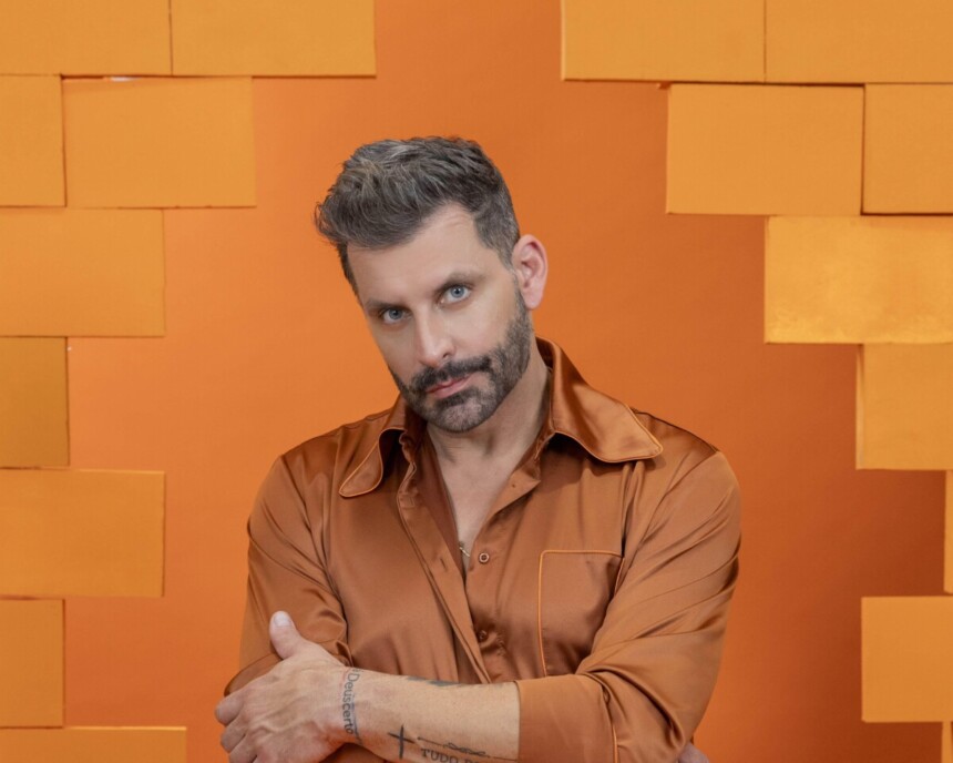 Henri Castelli veste roupa laranja e olha com olhar sério em foto oficial do BBB 26