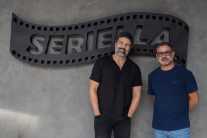 Carlos Manga Jr. ao lado de um homem de camisa azul em frente o logo da Seriella