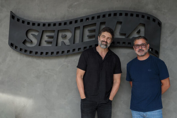 Carlos Manga Jr. ao lado de um homem de camisa azul em frente o logo da Seriella