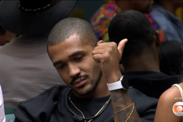 Matheus sentado no sofá do BBB faz sinal de legal