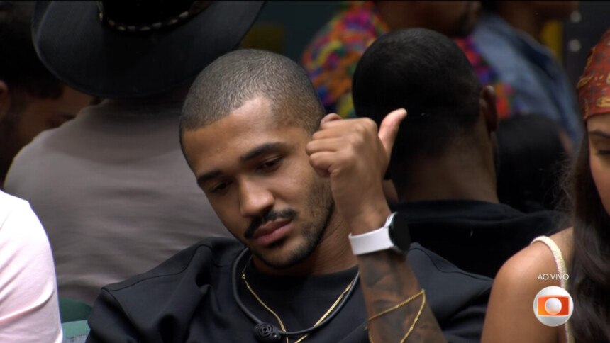 Matheus sentado no sofá do BBB faz sinal de legal