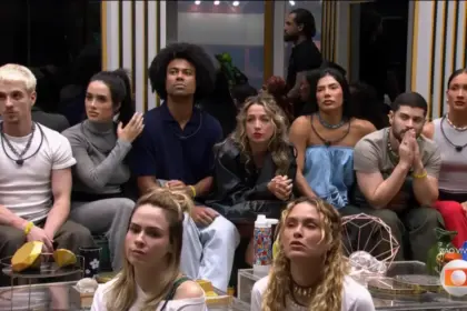 Participantes do BBB 26 sentados no chão da sala do programa antes da eliminação de Matheus. Eles olham para o telão