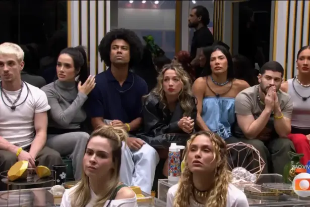 Participantes do BBB 26 sentados no chão da sala do programa antes da eliminação de Matheus. Eles olham para o telão