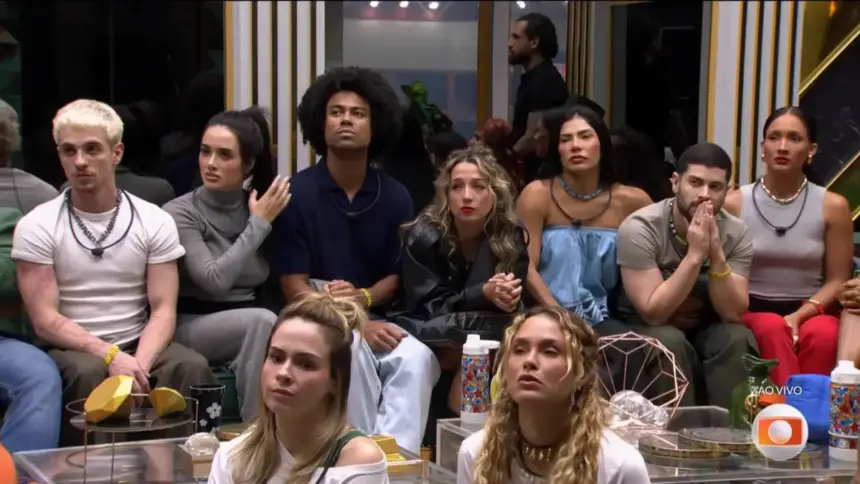 Participantes do BBB 26 sentados no chão da sala do programa antes da eliminação de Matheus. Eles olham para o telão