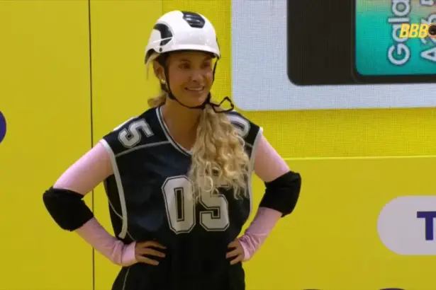 Sarah sorrindo com as mãos na cintura durante a prova do líder do BBB 26. Ela está com capacete branco