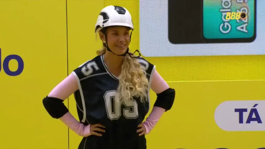 Sarah sorrindo com as mãos na cintura durante a prova do líder do BBB 26. Ela está com capacete branco