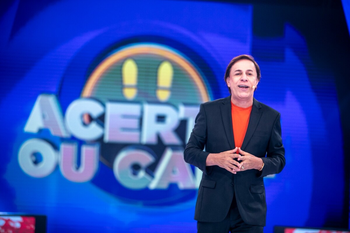 Tom sorridente na frente do telão com o logo do Acerte ou Caia
