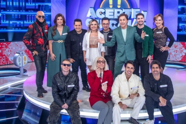 Tom Cavalcante com um terno verde musgo posa com os 11 participantes do reality show "Acerte ou Caia!" no palco, todos sorrindo e em clima de festa.