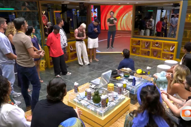 Alberto apresenta os brothers e sisters do seu VIP. Eles em pé olham para o telão da sala com Tadeu Schmidt