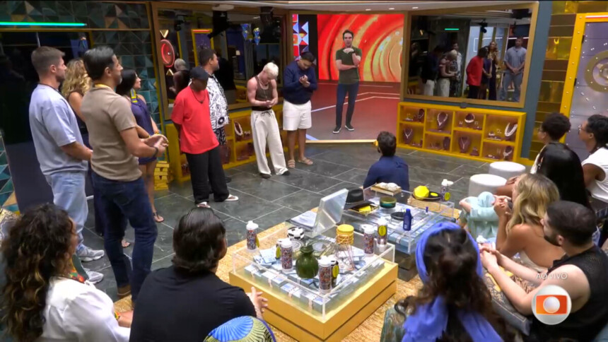 Alberto apresenta os brothers e sisters do seu VIP. Eles em pé olham para o telão da sala com Tadeu Schmidt