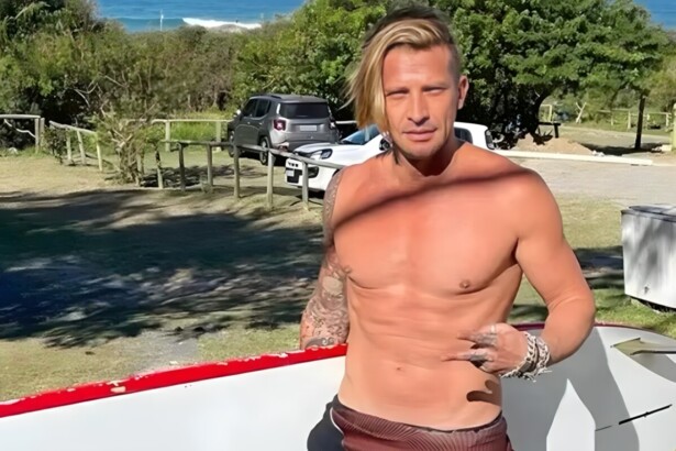 Álvaro Jacomossi segurando sua prancha de surf na areia de uma praia