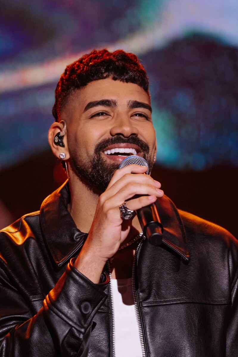 Dilsinho canta com os olhos fechados sorrindo no palco do Domingão