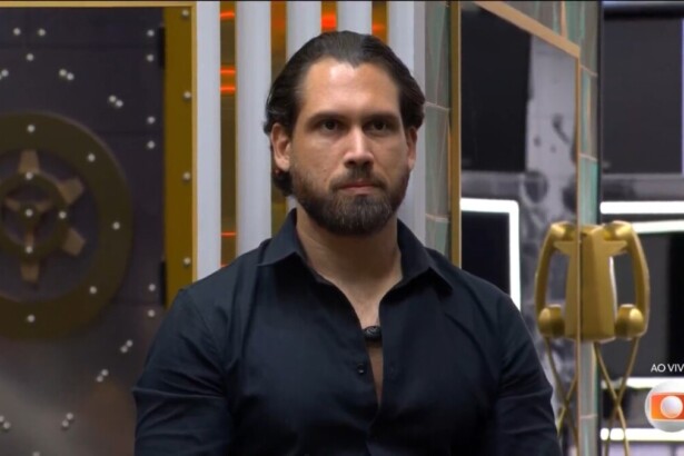 Brigido de camisa preta e semblante assustado ao descobrir que estava eliminado do BBB 26. Ele está sentado no sofá da sala