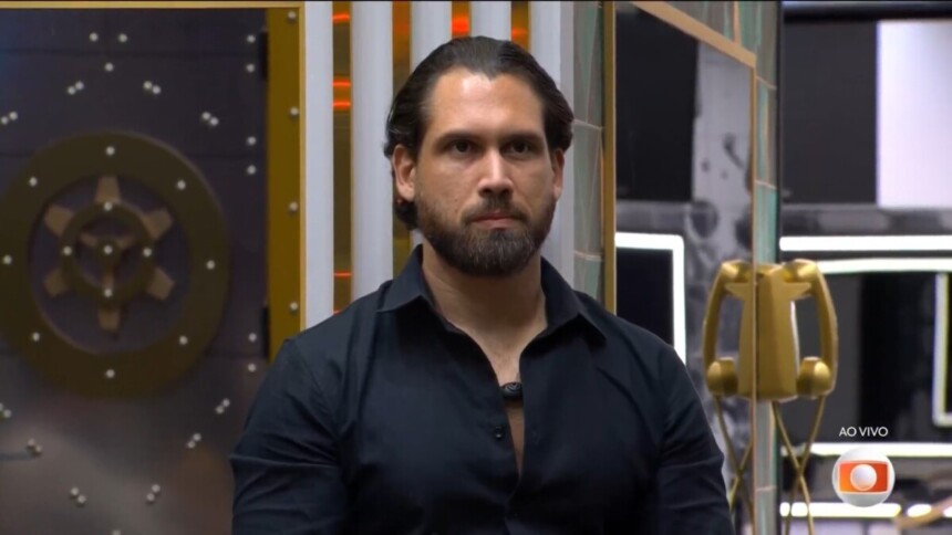 Brigido de camisa preta e semblante assustado ao descobrir que estava eliminado do BBB 26. Ele está sentado no sofá da sala