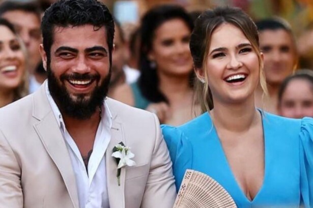 Cantor Henrique e a esposa Amanda sorridentes sentados durante um casamento