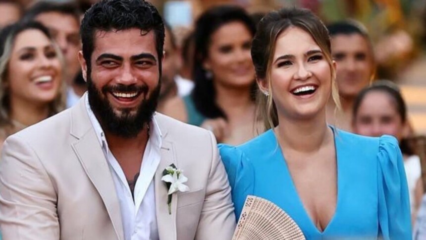 Cantor Henrique e a esposa Amanda sorridentes sentados durante um casamento