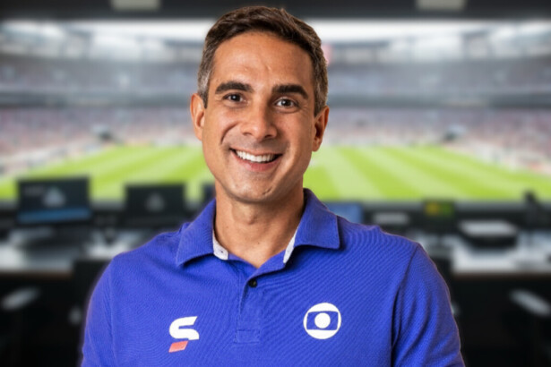 Gustavo Villani sorridente em uma cabine de transmissão de futebol ao vivo na Globo