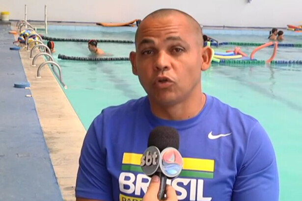 Adriano Gomes Lima sentado em uma cadeira de rodas em frente a uma piscina em entrevista ao microfone do SBT
