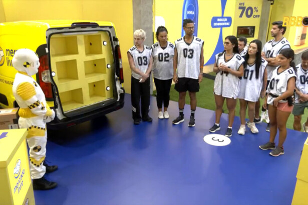 Dummie se posiciona ao lado de uma van no cenário da Prova do Anjo enquanto os participantes observam as instruções no BBB 26