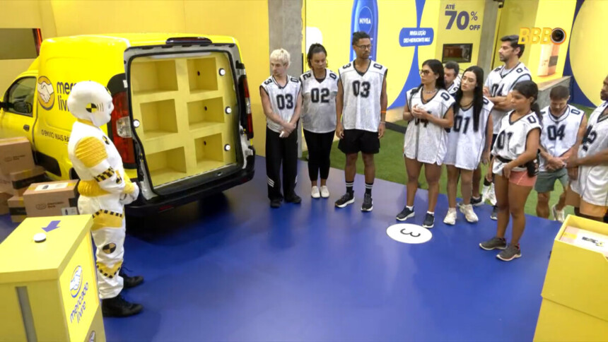 Dummie se posiciona ao lado de uma van no cenário da Prova do Anjo enquanto os participantes observam as instruções no BBB 26