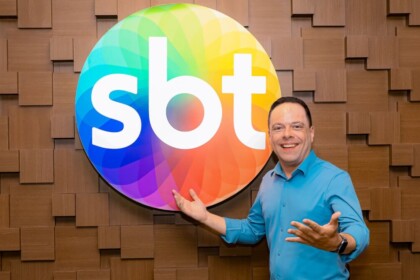 Thiago Gardinali sorridente em frente a logo do SBT