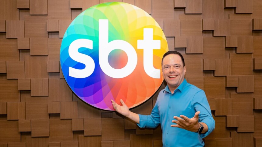 Thiago Gardinali sorridente em frente a logo do SBT