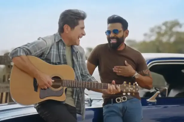 Daniel segura um violão e sorrir ao lado de Pablo que está em pé no carro