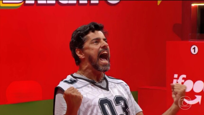 Alberto Cowboy com a boca aberta gritando e levantando os braços jogado ao chão da Prova do Líder do BBB 26