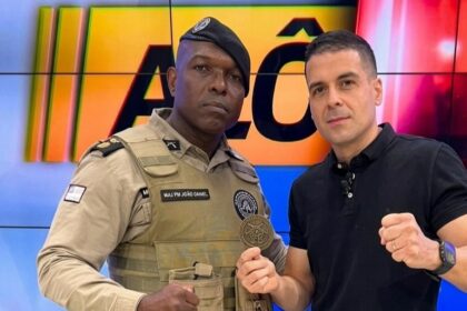 Marcelo Castro, o Juca, segura medalha ao lado do PM no estúdio do programa Alô Juca da TV Aratu, afiliada do SBT. Ambos estão com semblante sério
