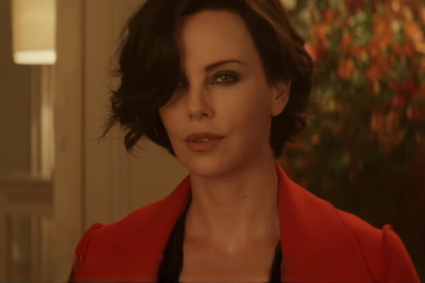 Charlize Theron vestida com um sobretudo vermelho, de cabelo curto e com uma arma em mãos em cena do filme Atômica