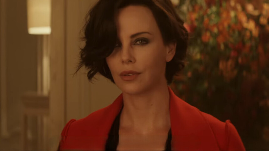 Charlize Theron vestida com um sobretudo vermelho, de cabelo curto e com uma arma em mãos em cena do filme Atômica