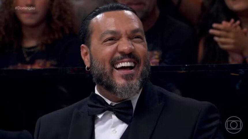 Belo, de terno e gravata borboleta, sorrindo, em trecho do Domingão