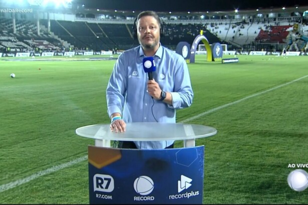 Bruno Laurence segura microfone da RECORD na bancada do Brasileirão montada no meio do campo de futebol
