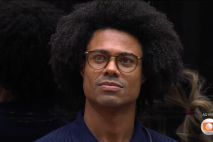 Breno usa óculos e olha para o telão do BBB 26