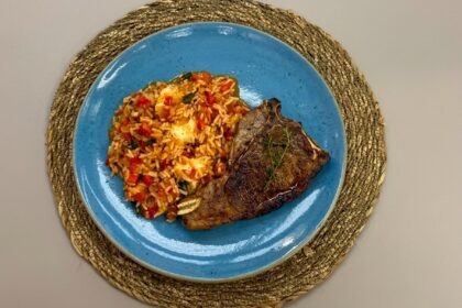 Chuleta na frigideira com arroz de tomate em um prato azul em cima da mesa do É de Casa