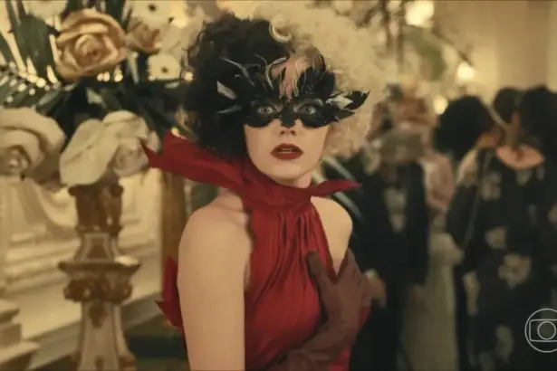 Emma Stone como Cruella, usando um vestido de galla vermelho e assustada em cena do filme da Disney