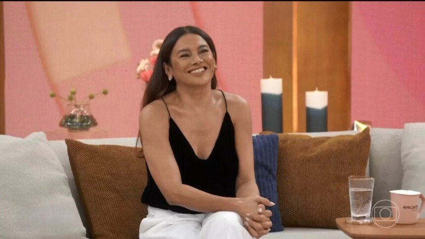 Dira Paes sorridente sentada no sofá do programa Encontro