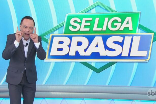 Thiago Gardinali aponta os dois dedos para cima no cenário do Se Liga Brasil no SBT comemorando a alta audiência. Ele está sorridente
